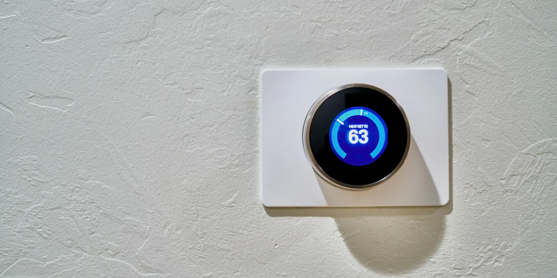 A round smart thermostat on a white wall plate, set to 63 degrees
